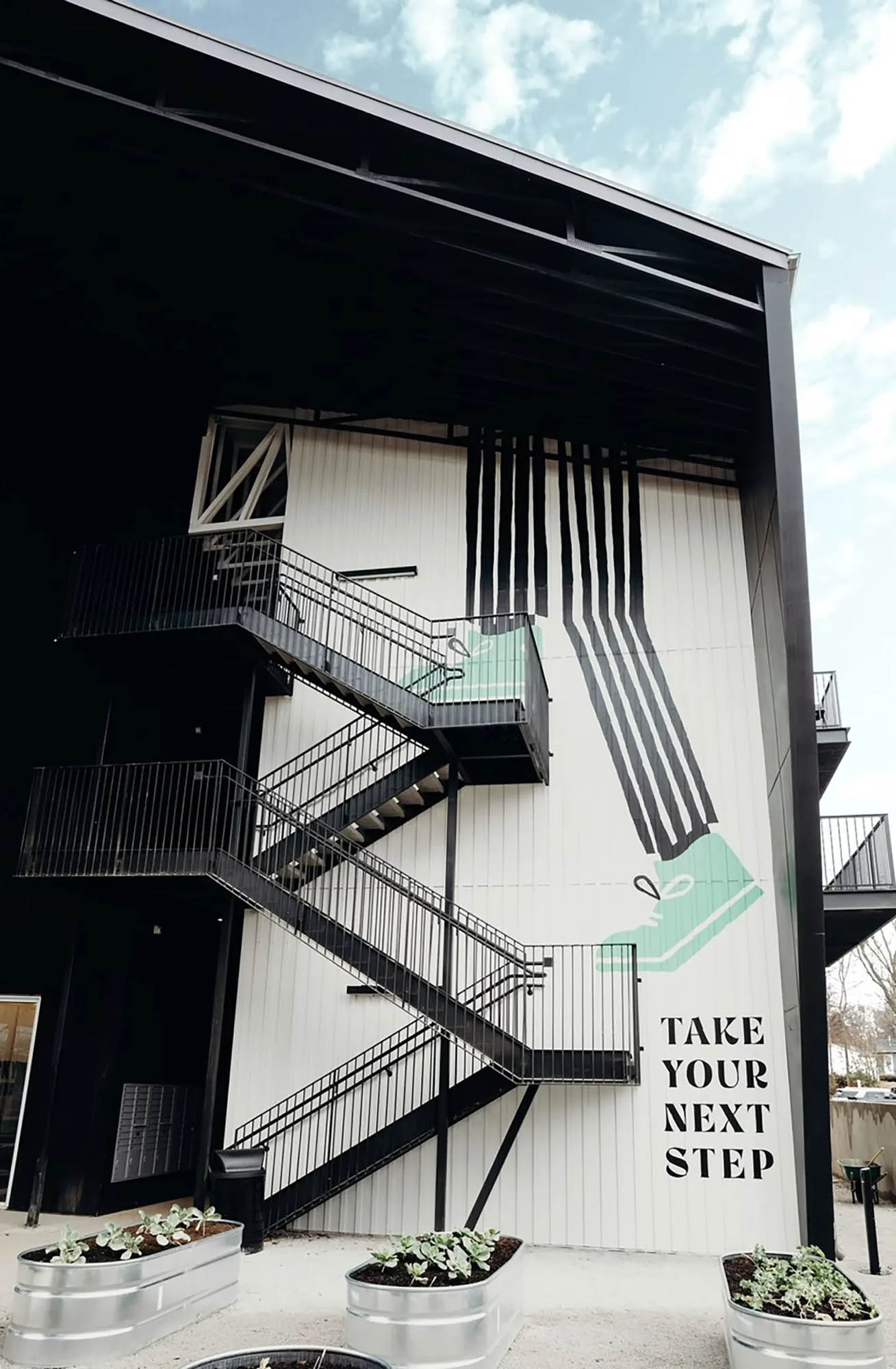 Artful mural on the side of apartment staircase that says Take Your Next Step