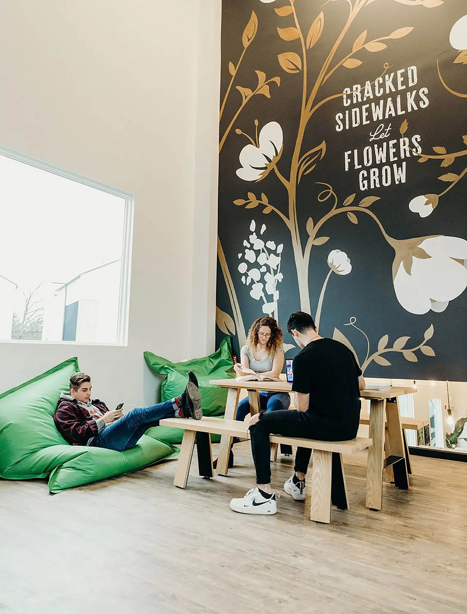 Three residents sitting in a loft or common space with green beanbag chairs and a floral wall mural