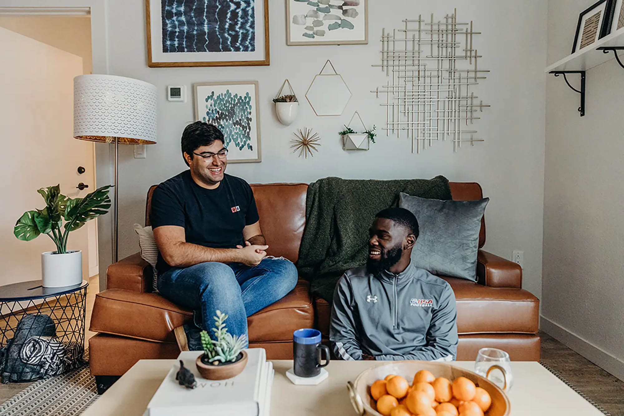 Two men sitting on a leather couch with a gallery of art behind them