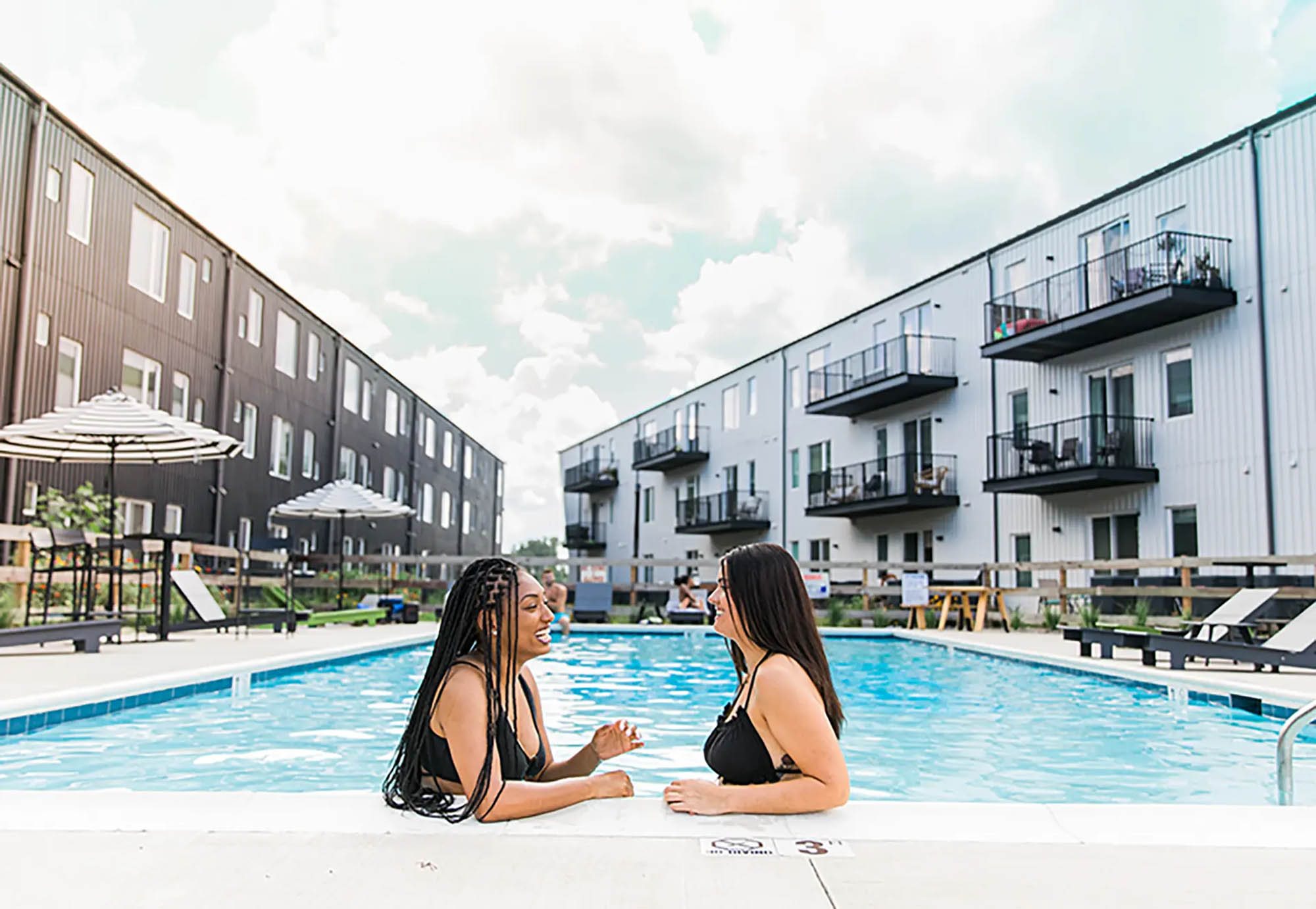 Two women sitting in a pool smiling and talking